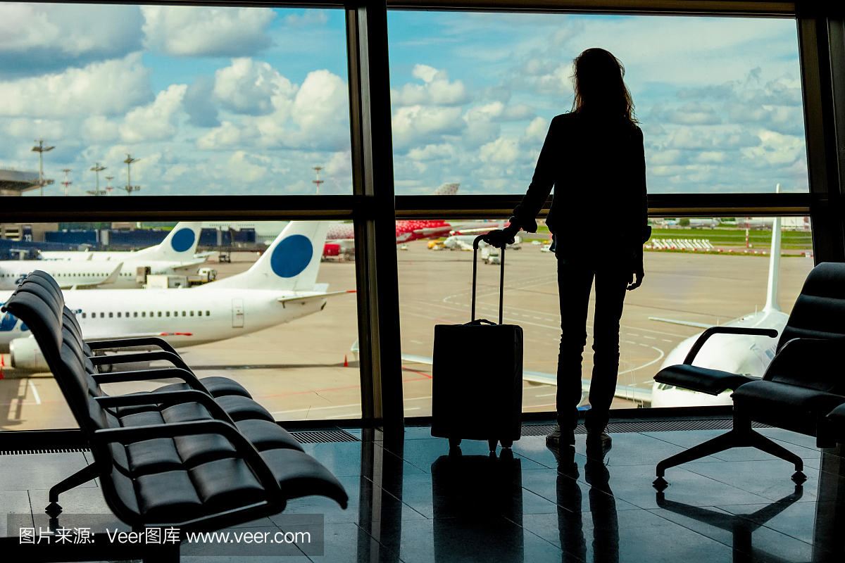 那个女人的剪影,那个旅客拿着行李站在机场靠近窗口的地方